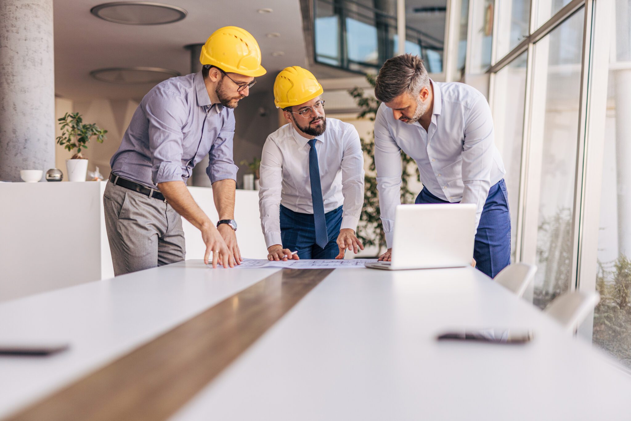 Three professionals in hard hats discussing project plans on a conference table, emphasizing collaboration and clear communication in consulting and copywriting.